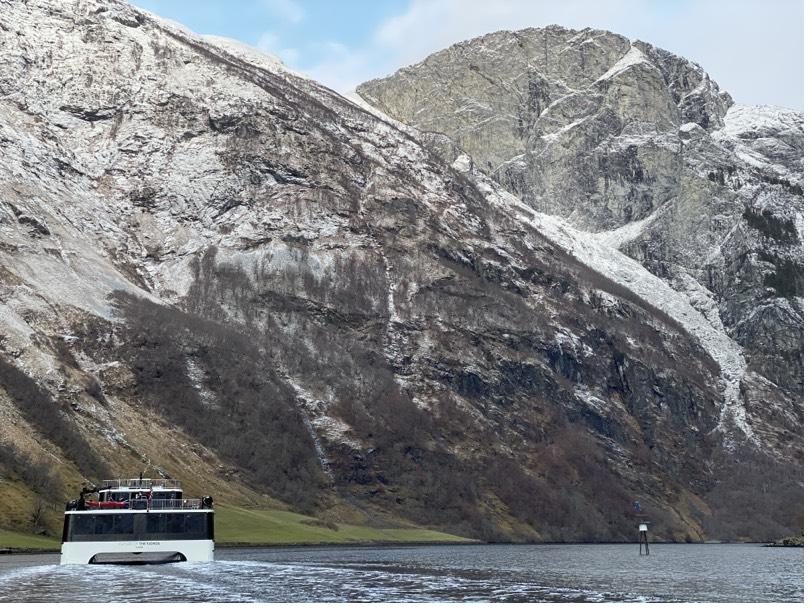 A small passenger boat on the fjord beneath snow-dusted cliffs